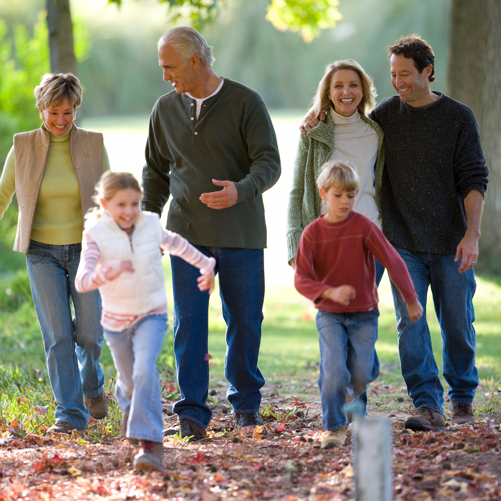 Portrait complet d'une famille multi- générationnelle marchant dans un parc avec des couples en étreinte et des enfants en train de courir devant pendant une journée ensoleillée en automne.